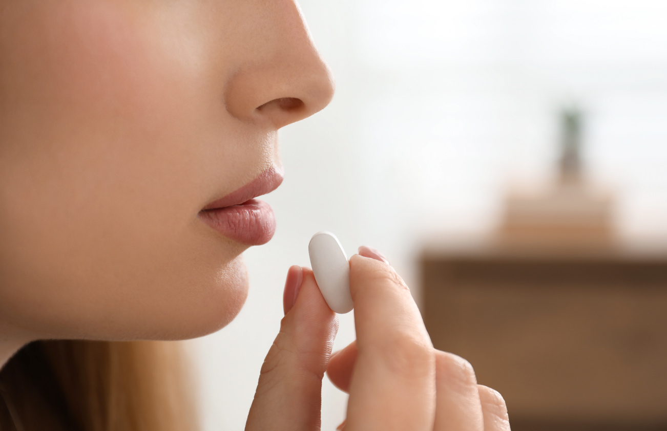 Young Woman Taking Abortion Pill on Blurred Background, Closeup